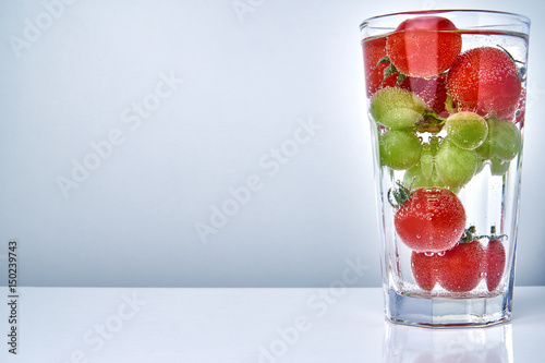Фотография Cherry tomatos and grapes in a cocktail glas in water with copy space