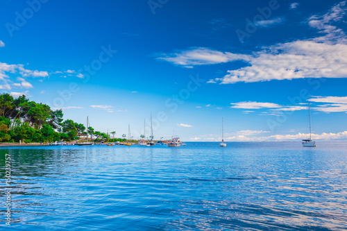 Wonderful romantic summer landscape panorama coastline sea. Boats and yachts in harbor at cristal clear azure water. Green trees at the edge of the coast. © Sodel Vladyslav