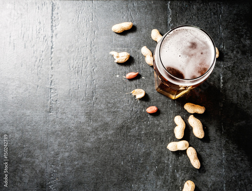Glass of beer and snack of peanuts on a concrete table