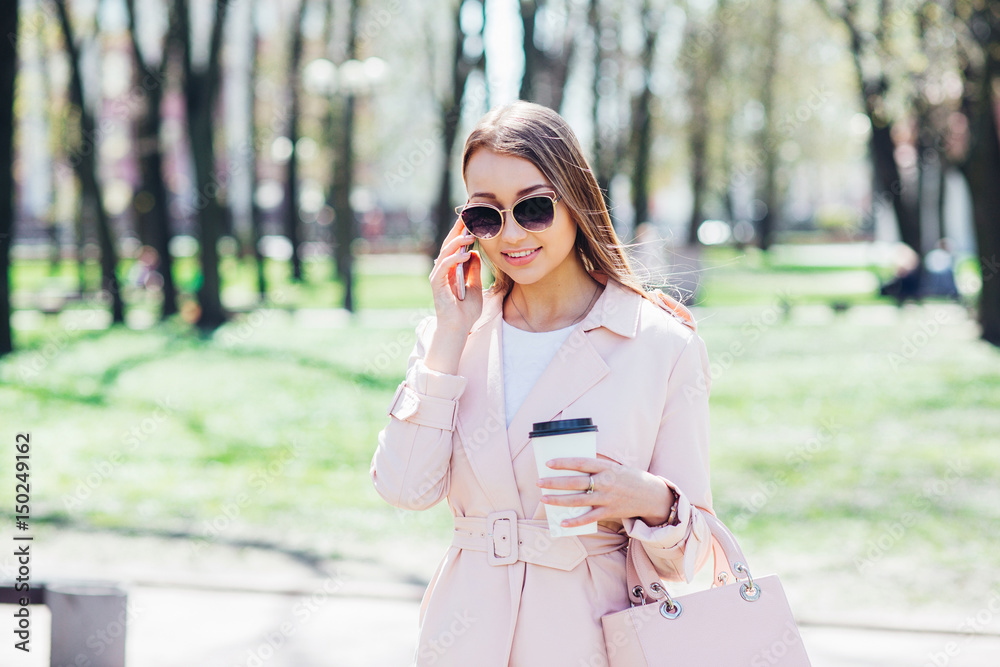 Fashionable woman with phone and cofee in the city. Fashion woman in a sunglasses and pink jacket outdoor