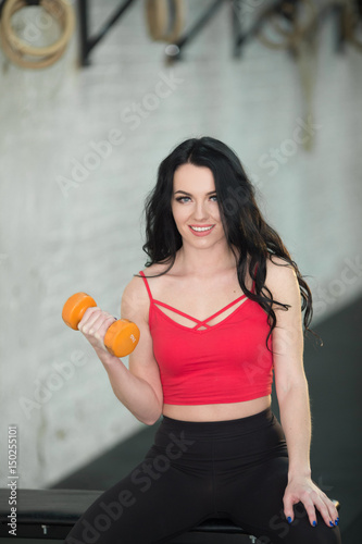 Beautiful young girl is exercising in the gym with dumbbells