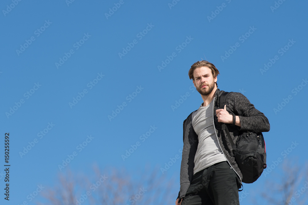 thoughtful young man against blue sky background with sport bag