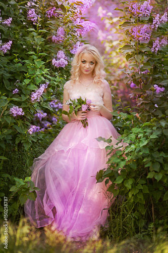 Beautiful woman enjoying lilac garden, young woman with flowers in green park. cheerful teenager walking outdoor. soft light style color.Young girl in beautiful wreath of lilac flowers