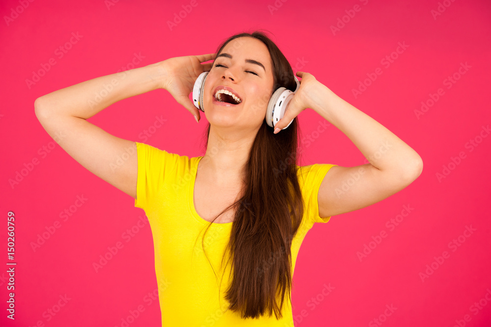 Beautiful young woman in black and yellow vibrant dress dances as she listens to the music over pink background Beautiful young woman in black and yellow vibrant dress dances as she listens to the music over pink background