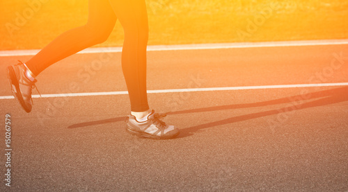 Shallow depth of field, toned with instagram like filter, flare effect. Closeup of female in running shoes going for run on road at sunrise or sunset. Toned.