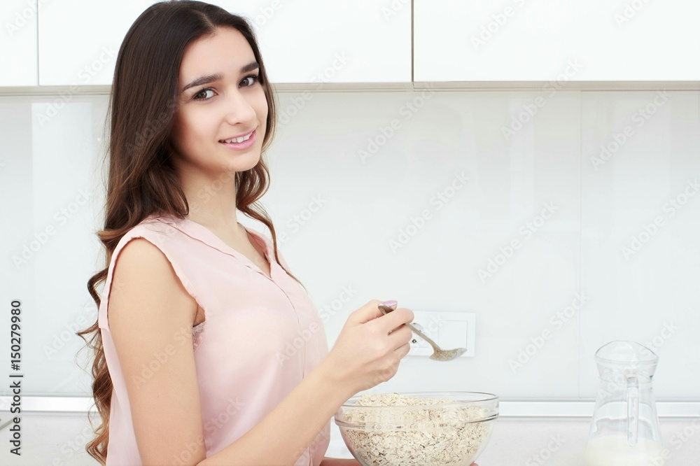 Healthy breakfast . Young beautiful cheerful woman putting cereal in a bowl while sitting on the worktop and smiling.