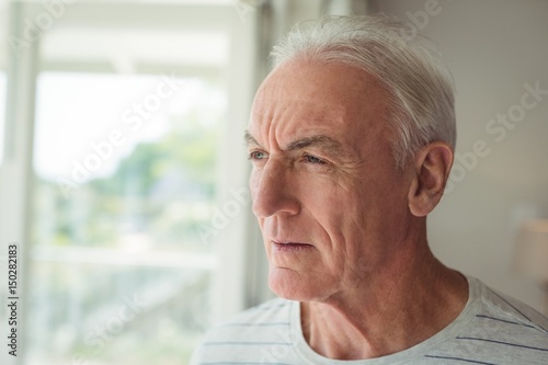 Thoughtful senior man standing next to window