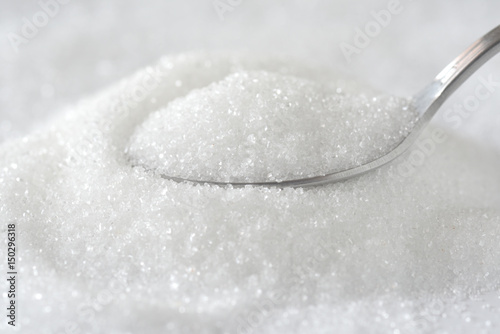 Spoon with white granulated sugar on white texture background. Unhealthy food concept.