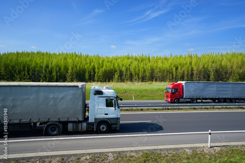 Passing trucks on a highway along a larch forest in the countryside