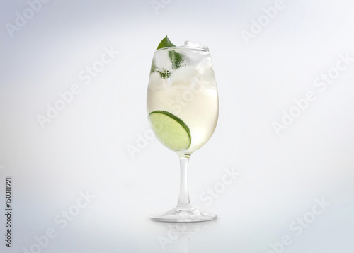 Glass of a cold cocktail drink with white wine / vermouth, slice of lemon / lime and a mint leaf. Isolated on white background. 