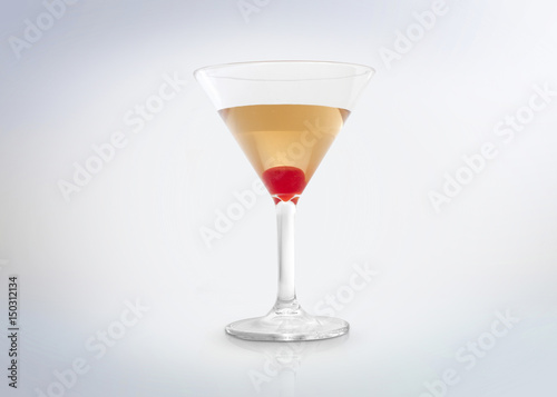 Glass of a gold / yellow / amber cocktail drink with a red cherry on the bottom. Isolated on white background. 