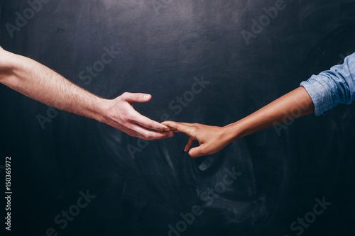 Reconnection of relationship or breakup.Two hands hold each other. Unrecognizable white guy and black woman on a dark background holding hands.