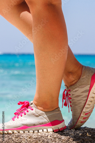 Runner woman stands on a rock near the blue sea. Red laces gray sneakers. Closeup. Photo knee © dadoodas