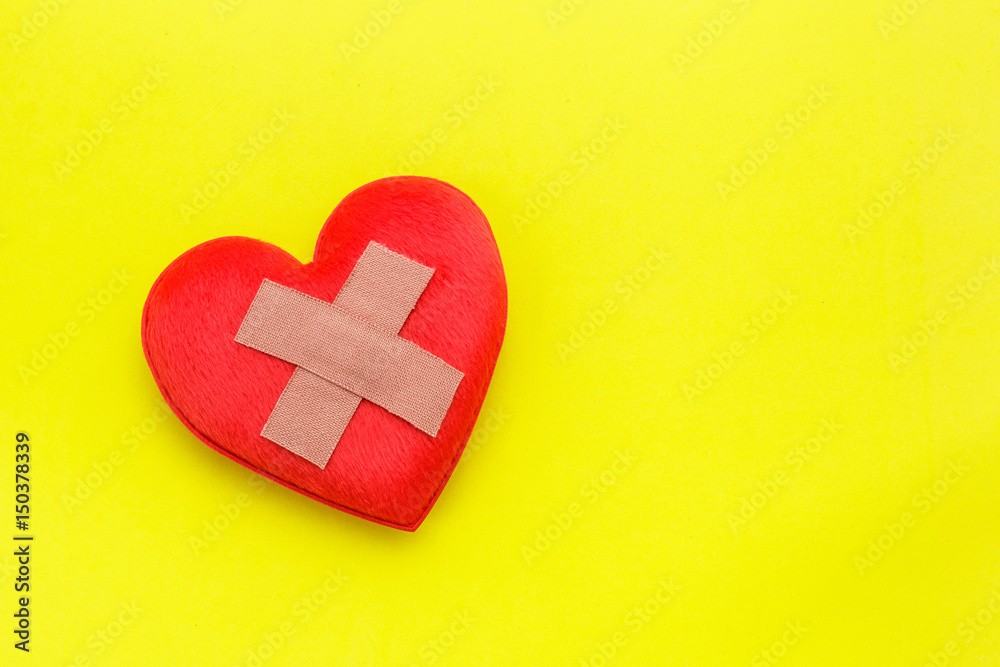Plaster or band-aid on red heart shape on yellow background. Use for heart problem or illness concept Plaster or band-aid on red heart shape on yellow background. Use for heart problem or illness concept
