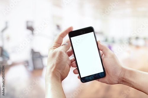  Man using smartphone in fitness gym background. Blank screen tablet for graphic display montage.