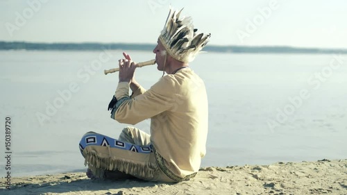 An Indian in a national costume plays a flute on the river bank 4k