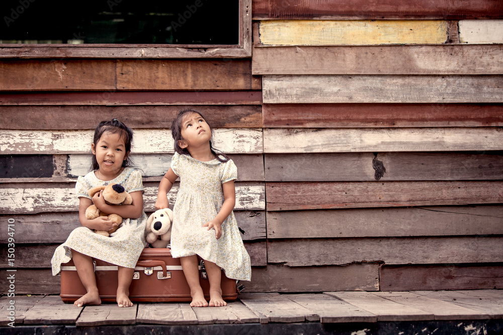 children two cute asian little girls are sitting on suitcase and playing together on wooden background in vintage retro style children two cute asian little girls are sitting on suitcase and playing together on wooden background in vintage retro style