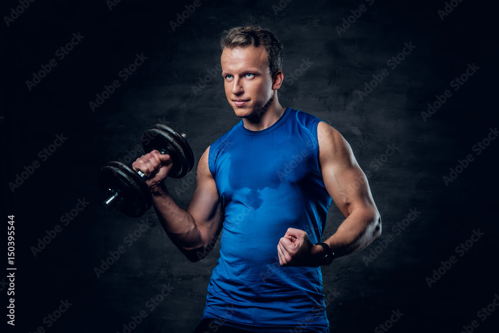 Athletic male in a blue sportswear holds the dumbbell.