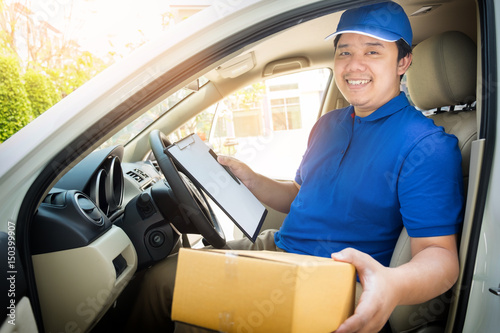 Delivery man with cardboard box checking document list In van and parcels on seat outside the warehouse