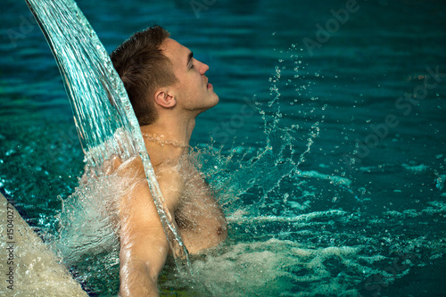 Handsome young cheerful man enjoying hydrotherapy at the spa pool
