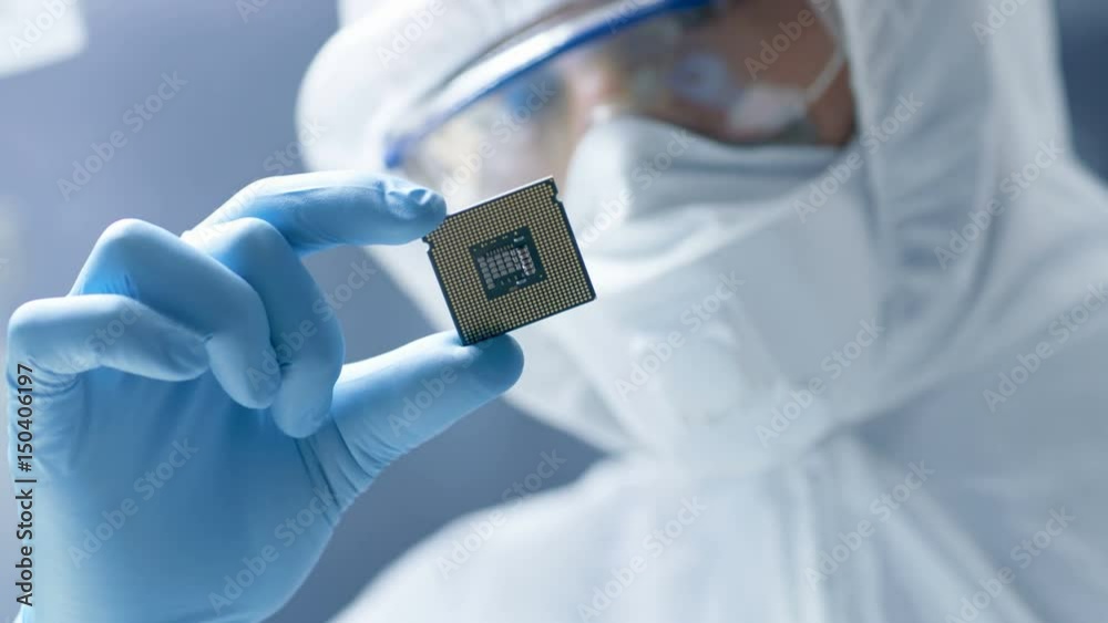 In Ultra Modern Electronic Manufacturing Factory Design Engineer in Sterile Coverall Holds Microchip with Gloves and Examines it. Shot on RED EPIC-W 8K Helium Cinema Camera.