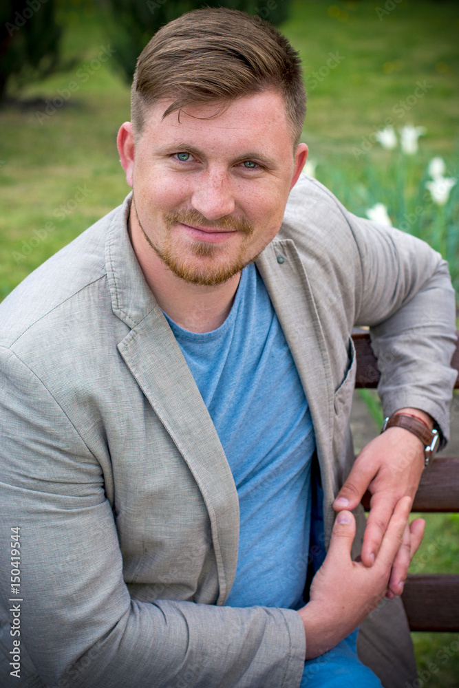 Portrait young man with light hair and  freckles. Man in city walk near park in grey Jacket and blue shirt