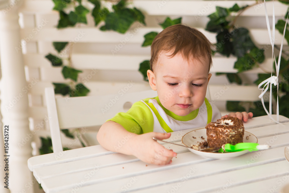 Happy little kid boy celebrating his birthday holds piece of cake, indoor. Birthday party for children. Carefree childhood, happiness. Two years old