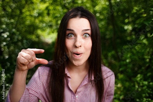Portrait of mocking or extremely surprised  of something small woman with wide-eyed face, showing small thing in a gesture photo