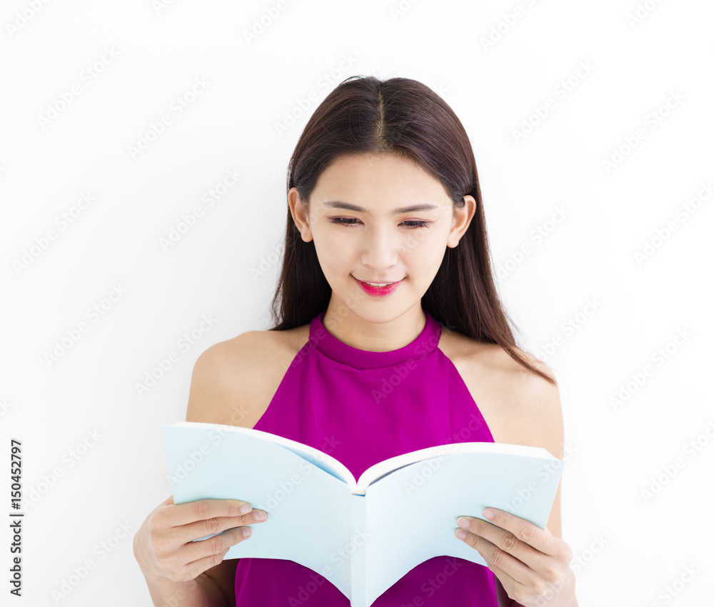 Smiling young woman reading book against white wall. Smiling young woman reading book against white wall.