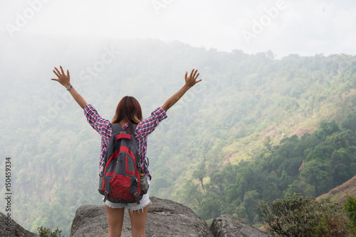 Hiker with backpack standing on top of a mountain with raised hands and enjoying nature view.