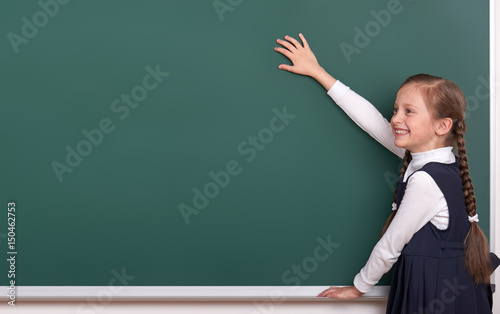 elementary school girl put hands on chalkboard background and show blank space, dressed in classic black suit, group pupil, education concept © soleg