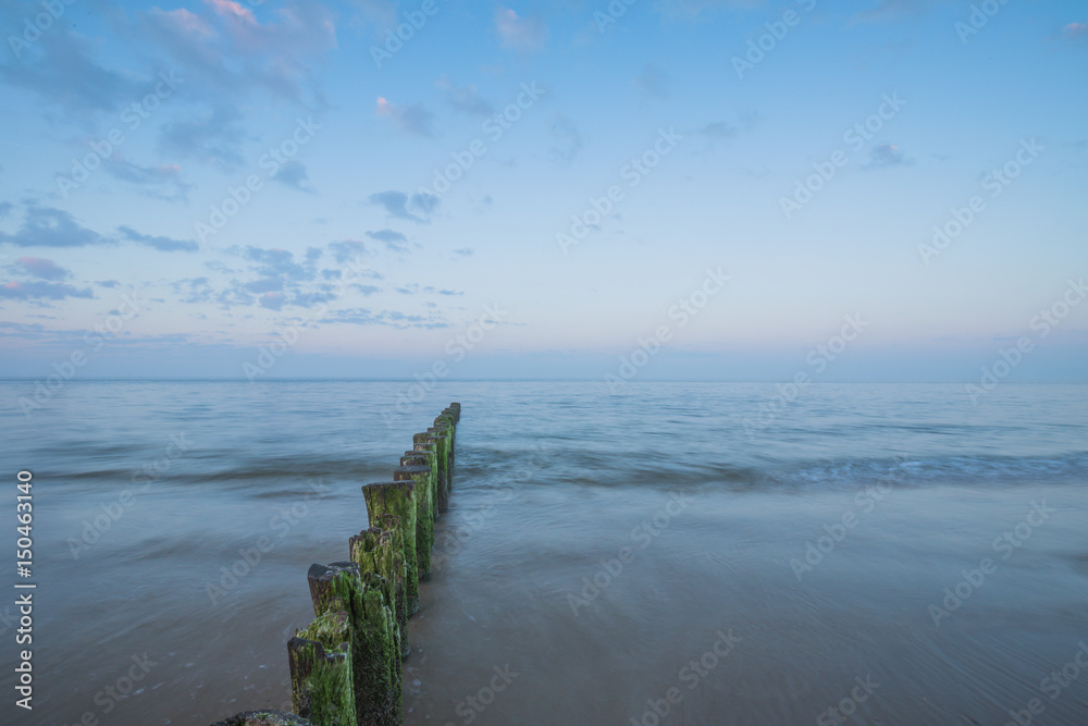 Wooden Piles With Algae Pattern At Beach During Sunrise- Wave Breaker