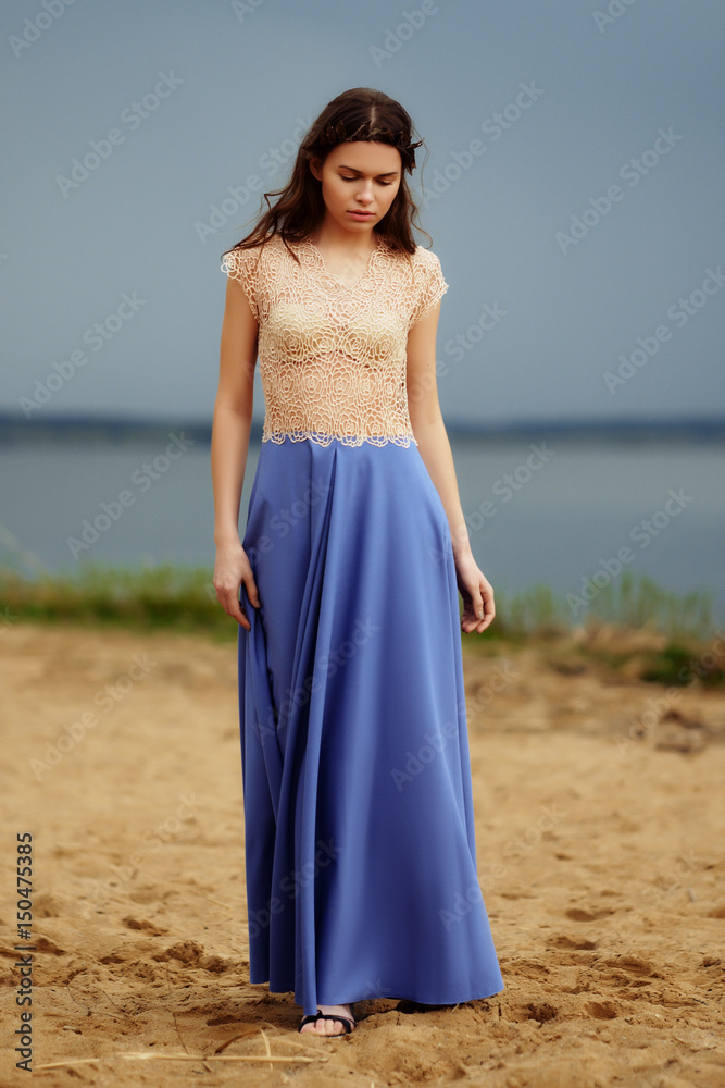 Calm lonely fashion model walking on the sand in a cloudy day. Romantic, gentle, mystical, image of a girl in long blue skirt and lace blouse. Calm lonely fashion model walking on the sand in a cloudy day. Romantic, gentle, mystical, image of a girl in long blue skirt and lace blouse.