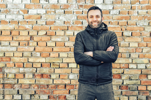 Close up portrait of happy man with beard smiling standing near a brick wall