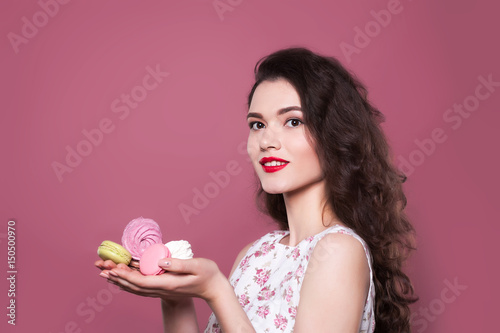 Beautiful young girl holds Macaroons and marshmallows on a pink background