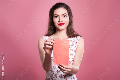 Beautiful girl with long hair keeps a red envelope on a pink background, space for text