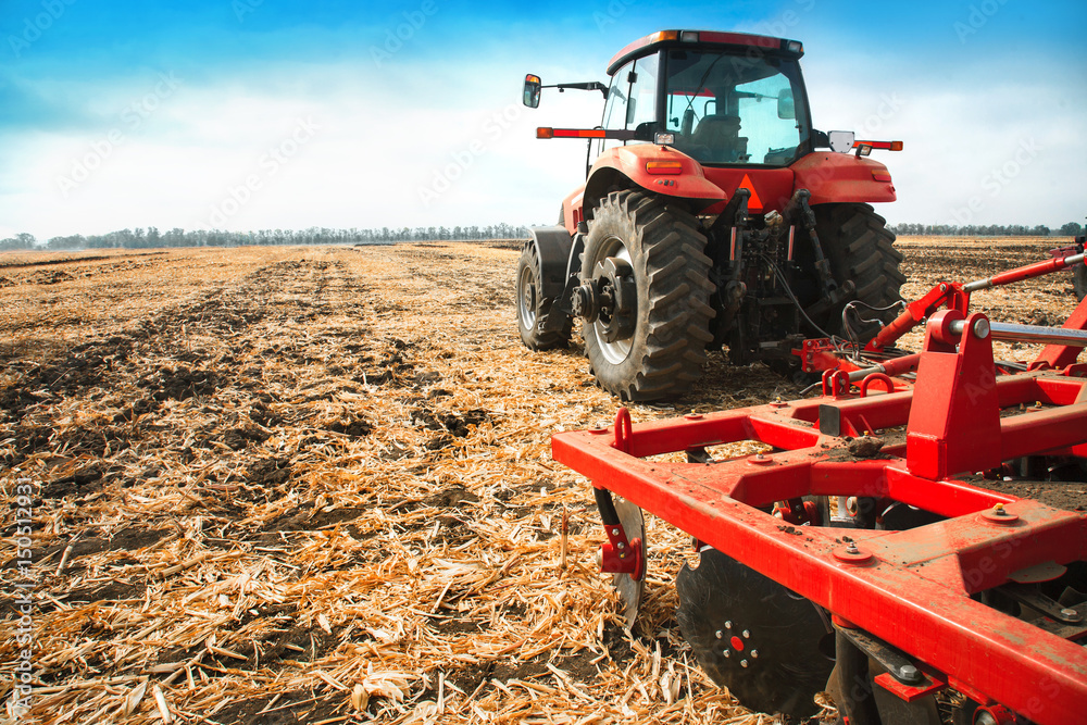 Obraz premium Red tractor in the field on a bright sunny day.