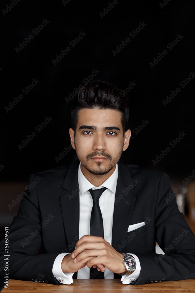 handsome confident young man in suit sitting in cafe, hands on the table. handsome confident young man in suit sitting in cafe, hands on the table.