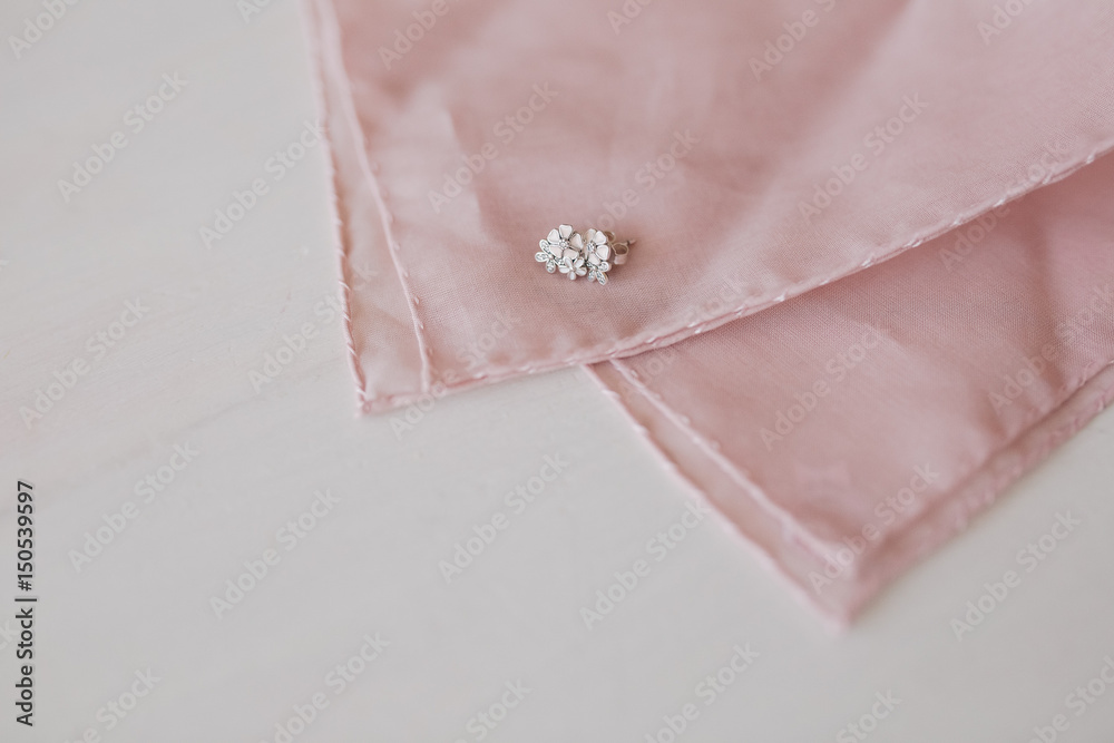 The bride's earrings in the shape of flowers lie on a pink shawl for the groom's jacket The bride's earrings in the shape of flowers lie on a pink shawl for the groom's jacket