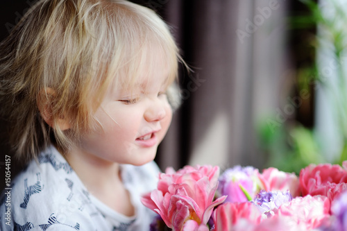 Cute blonde hair toddler smelling flowers at the home