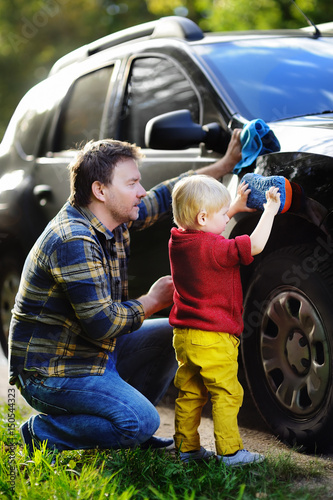 Middle age father with his toddler son washing car together outdoors