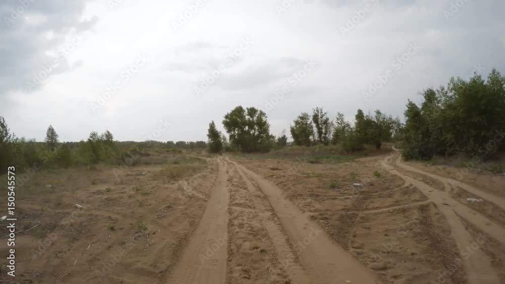 A view of the rural dirt road from camera installed on back of the car driving along this country road. Riding on a rough roadway. Traces of tires on the sand. A view of the rural dirt road from camera installed on back of the car driving along this country road. Riding on a rough roadway. Traces of tires on the sand.