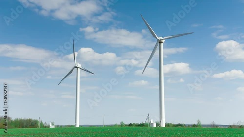Wallpaper Mural The blades of the two wind stations are spinning against the beautiful blue sky with feathery clouds on a sunny day. Two wind farms is white. Wind energy. Open green field. Torontodigital.ca
