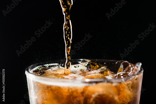 stream of cola is poured into a glass with ice