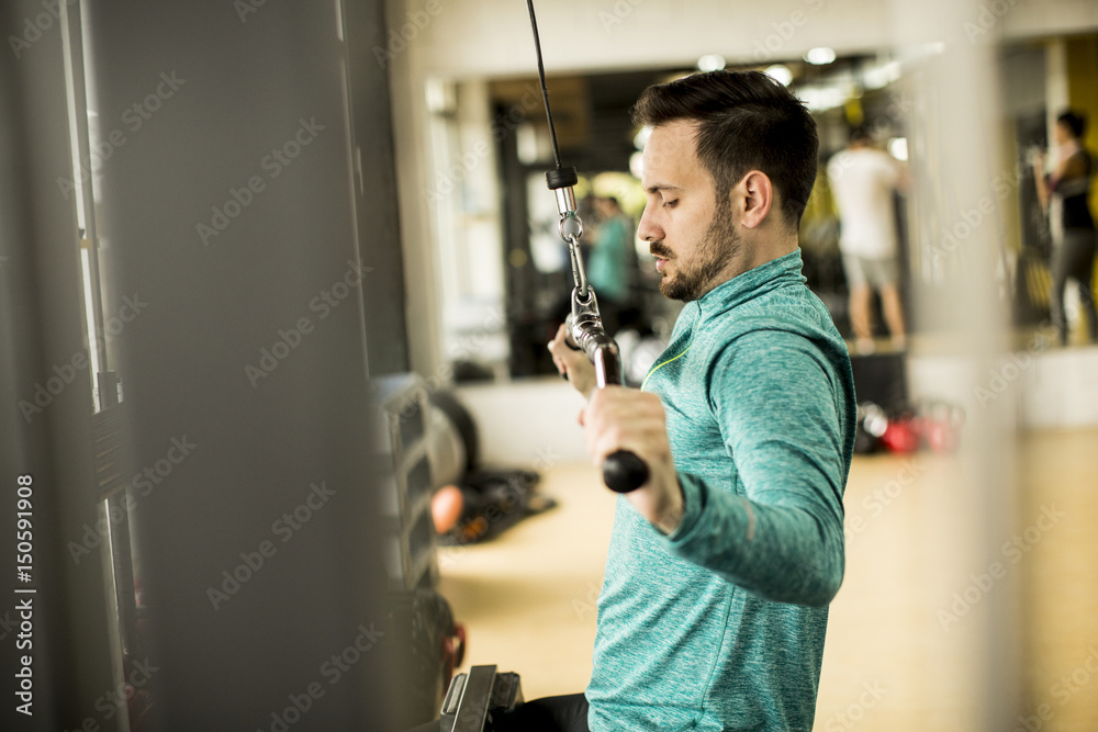 Young man doing exercise for triceps in the gym on mashine