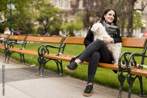 Bild auf Leinwand Young woman sitting in the park and holding a small dog in her lap