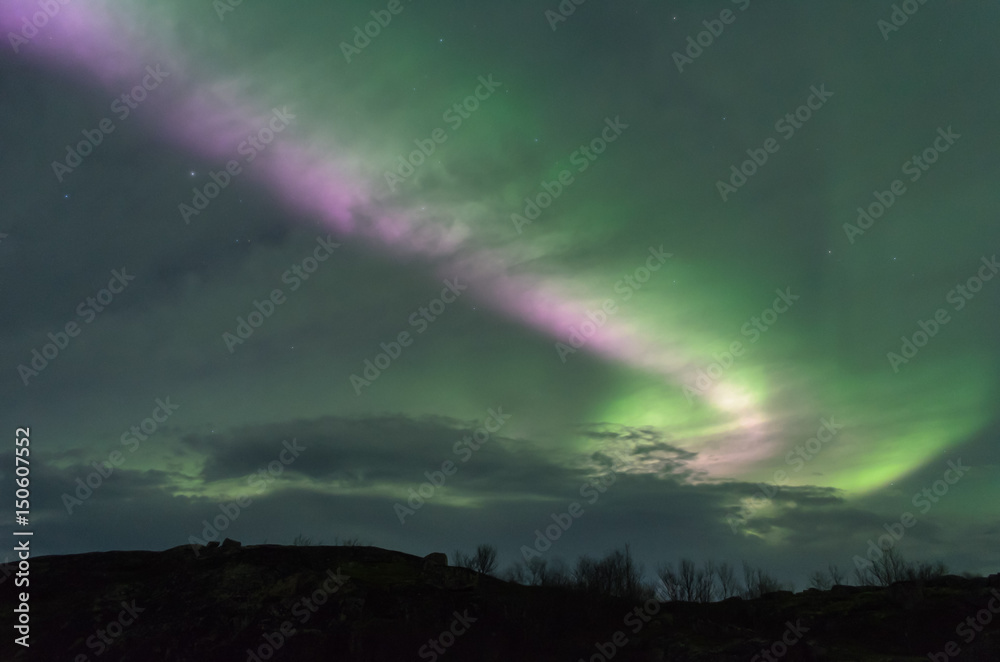 The Aurora and clouds in the sky above the hills .