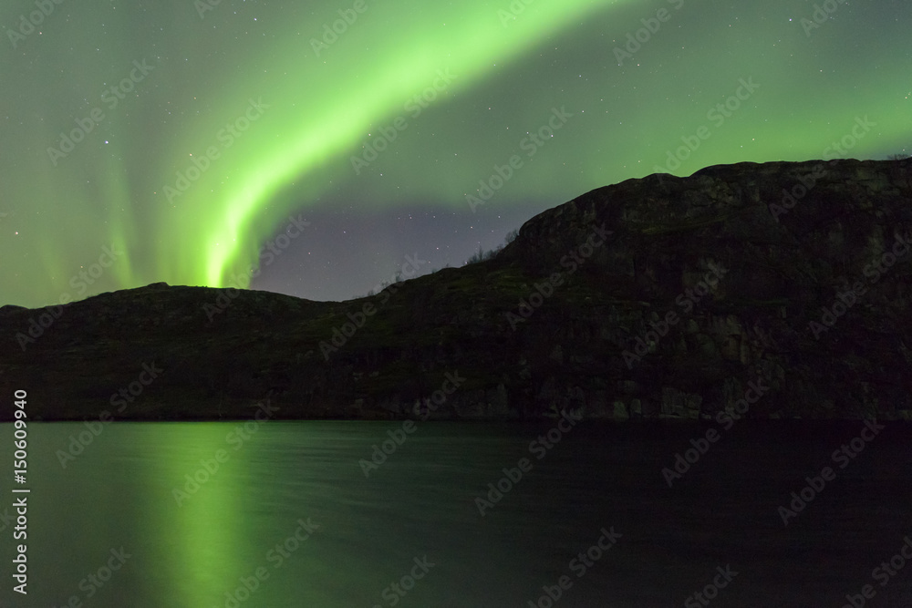 The Aurora in the sky above the hills . Reflected in the lake.