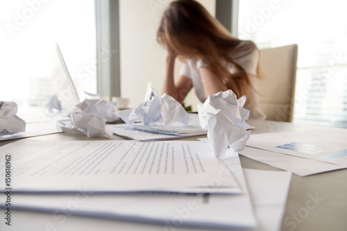 Bild auf Leinwand Businesswoman sitting with head in hands at desk covered crumpled papers