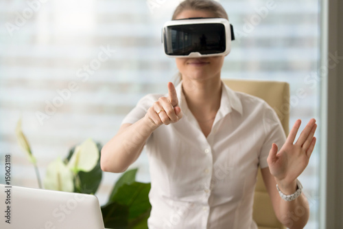 Woman in VR headset touching objects in virtual reality. Girl sitting in armchair at the desk and interacting with 3d visualization. Modern IT product test on digital simulator concept © fizkes
